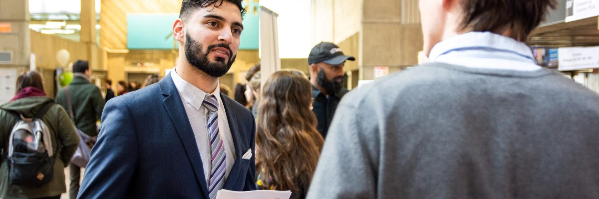younger man in suit talking to older man while holding resume