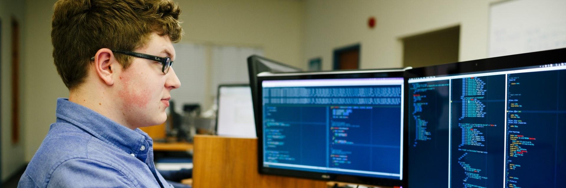 Person looks at two computer screens, with code on them.