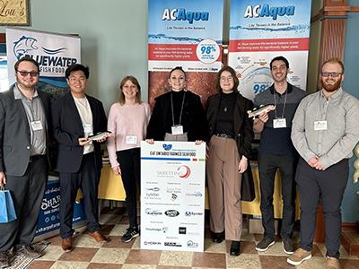 Dr. Huyben and students stand in a group photos at a conference with banners behind them.