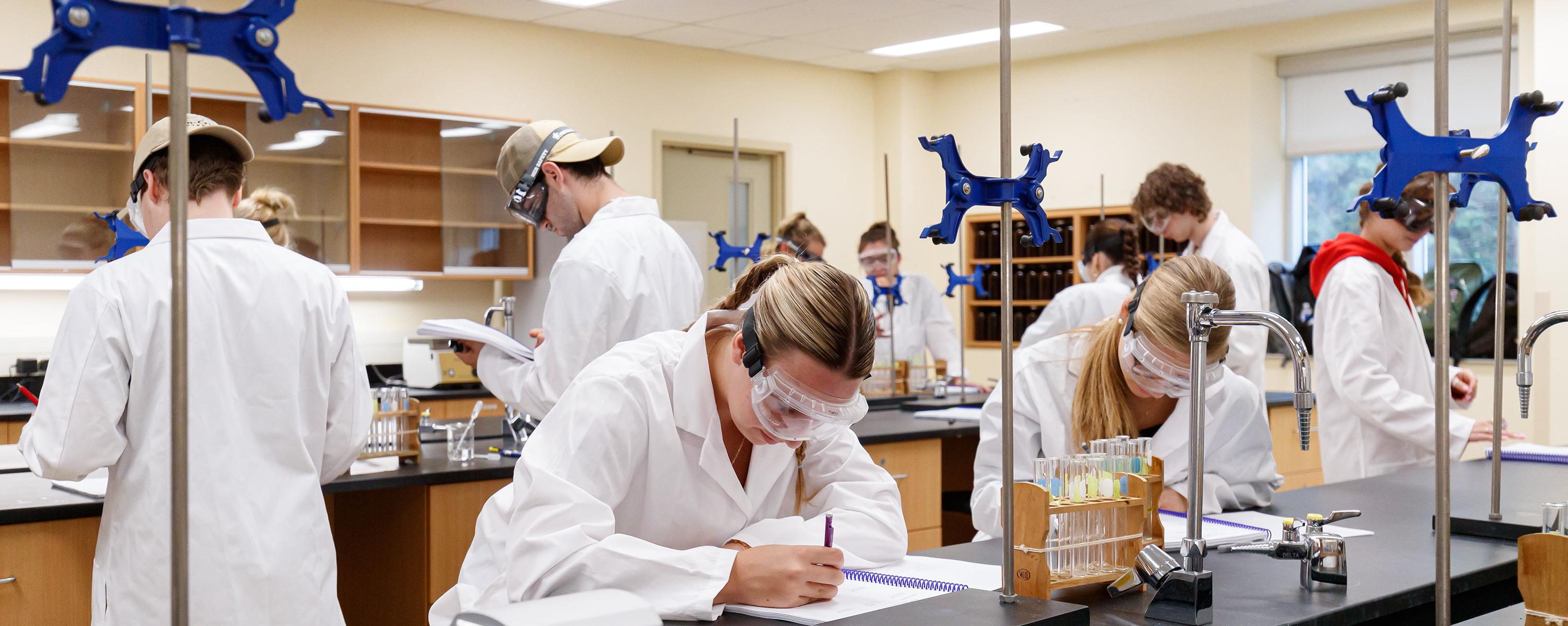 Group of students in Chem1040 lab wearing persona protective equipment and writing in notebooks