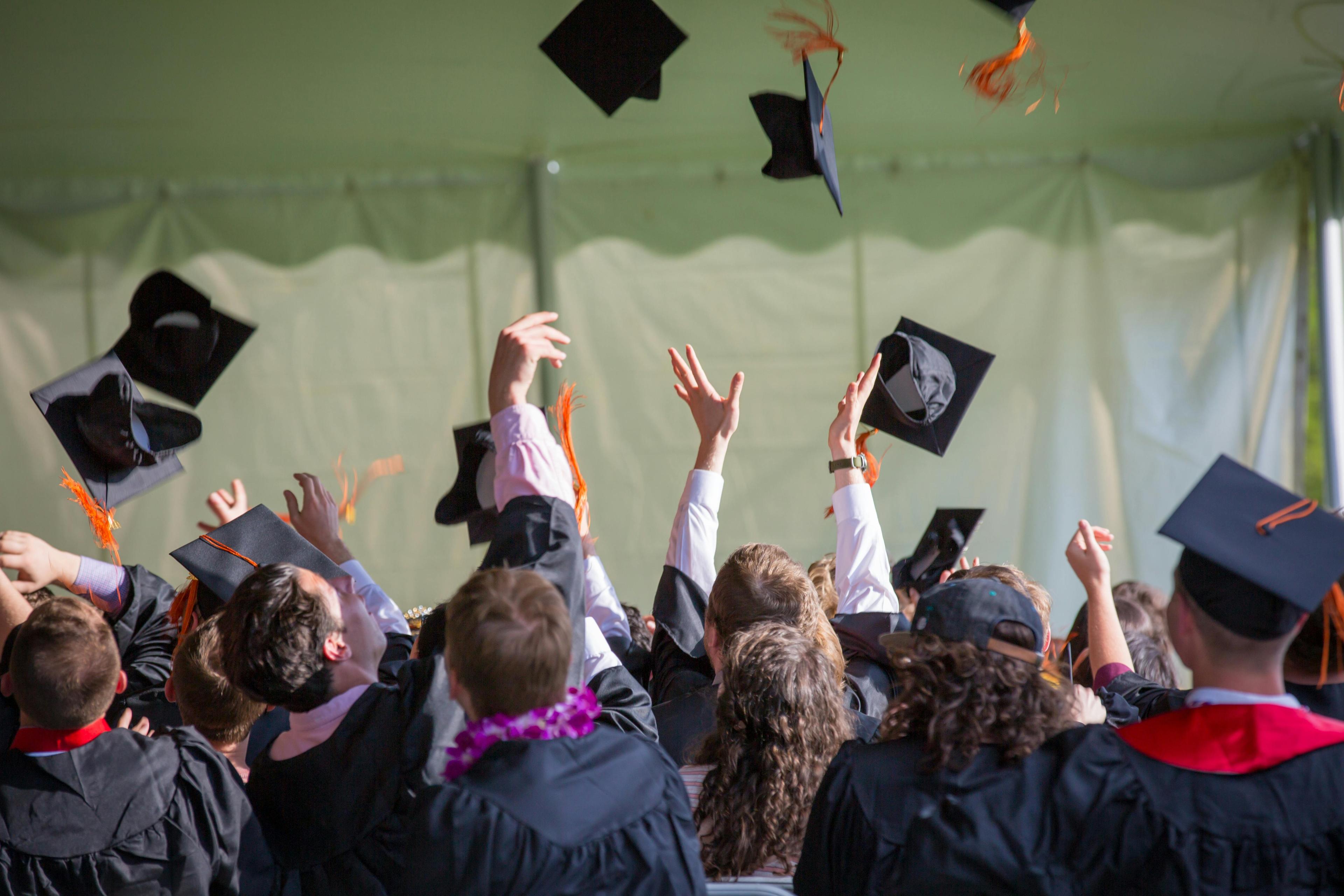 A group of graduates wearing gowns throw their caps in the air in celebration.