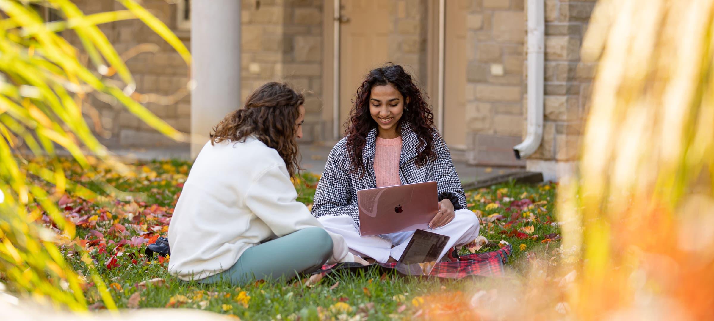 Two students sitting on grass and chatting outside the east residence