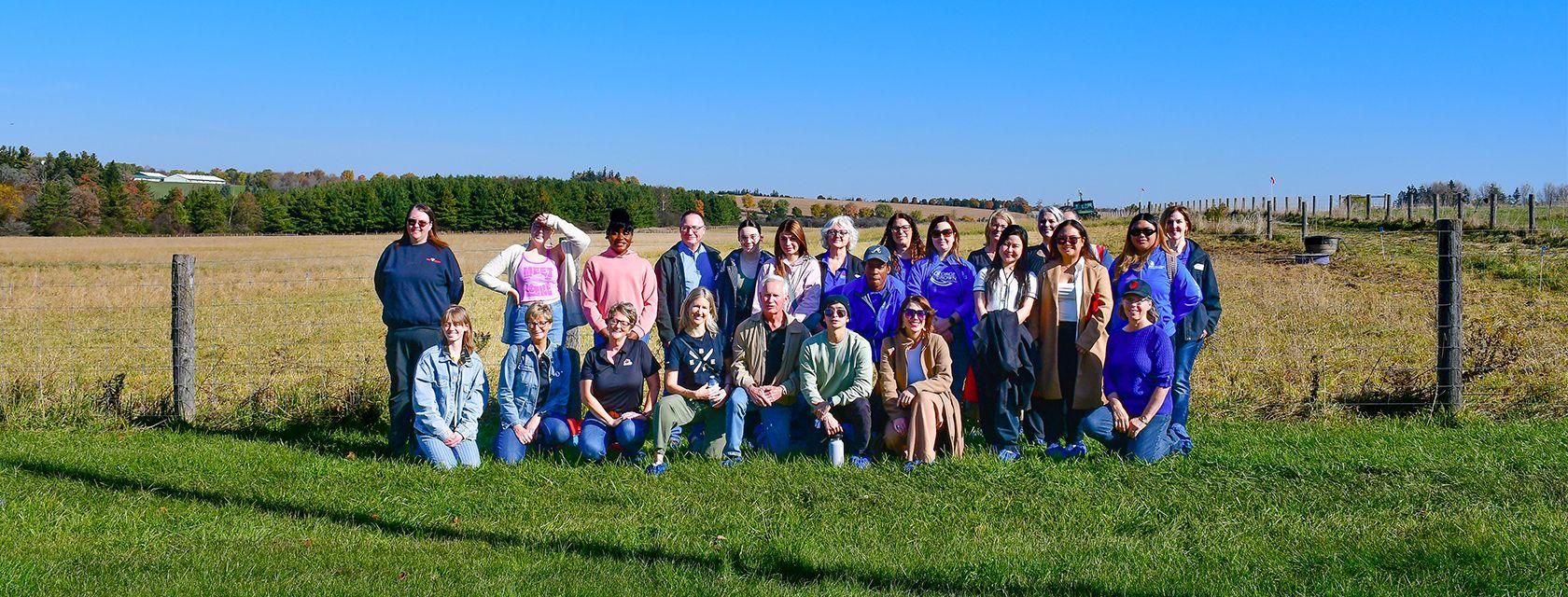 About 25 people post for a photo in front of a pasture at the Ontario Beef Research Centre as part of the 2024 culinary student tour