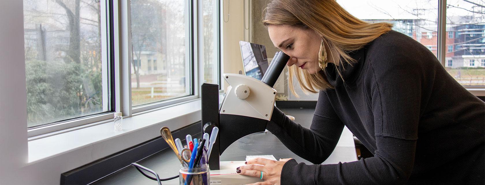 U of G Faculty looking through a microscope, focused on examining a specimen