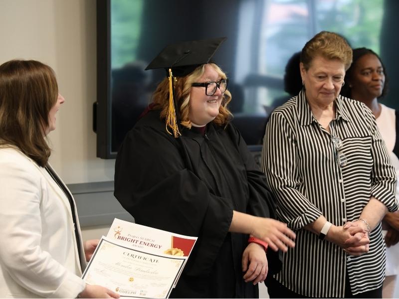 A graduating student smiles while waiting to receive an award certificate.