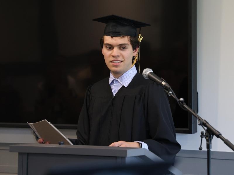 A graduating student stands at a podium to speak into a microphone.