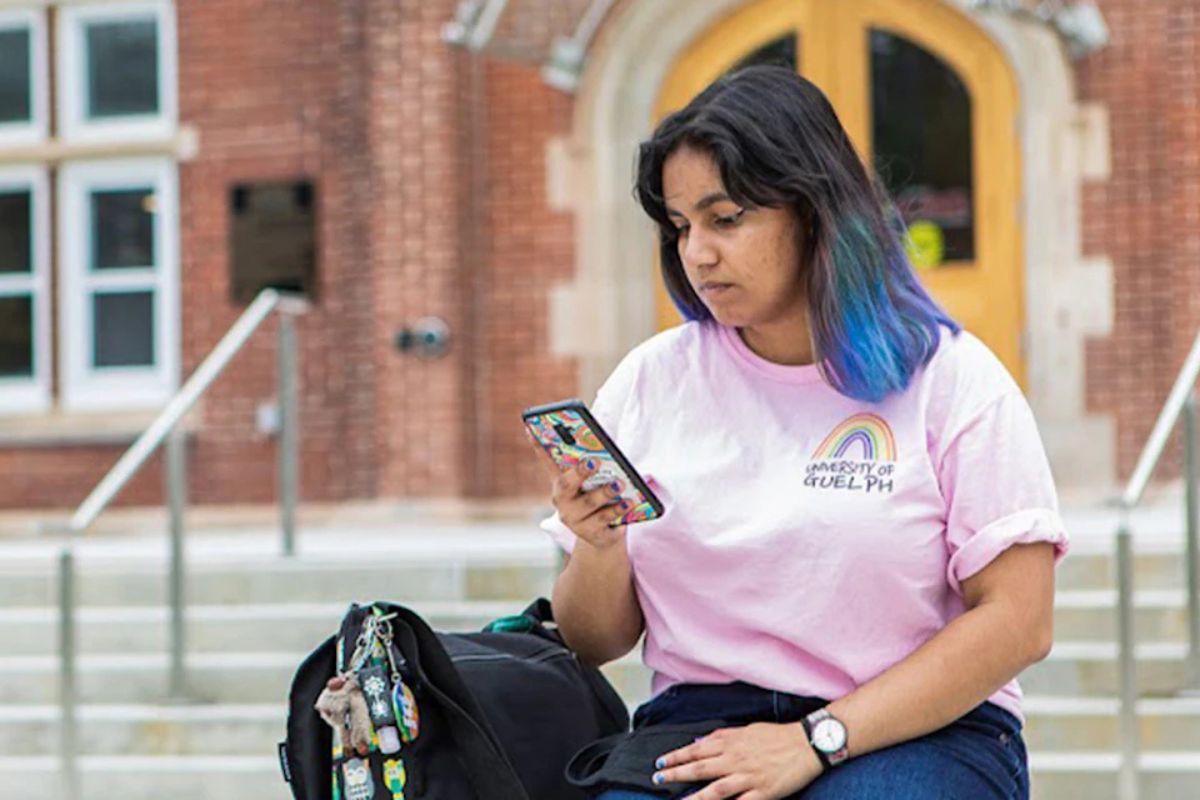 U of G student wearing a pink shirt sits looking at their phone.