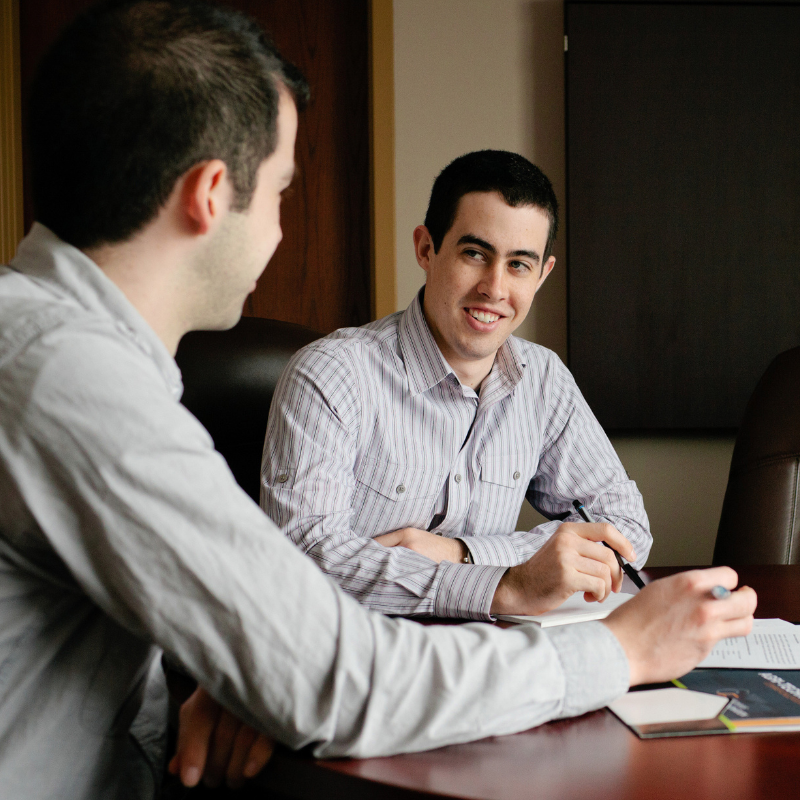 A student sits in a boardroom, chatting with his employer.
