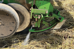 A high-pressure water jet sprays from a large machine into a residue-covered field
