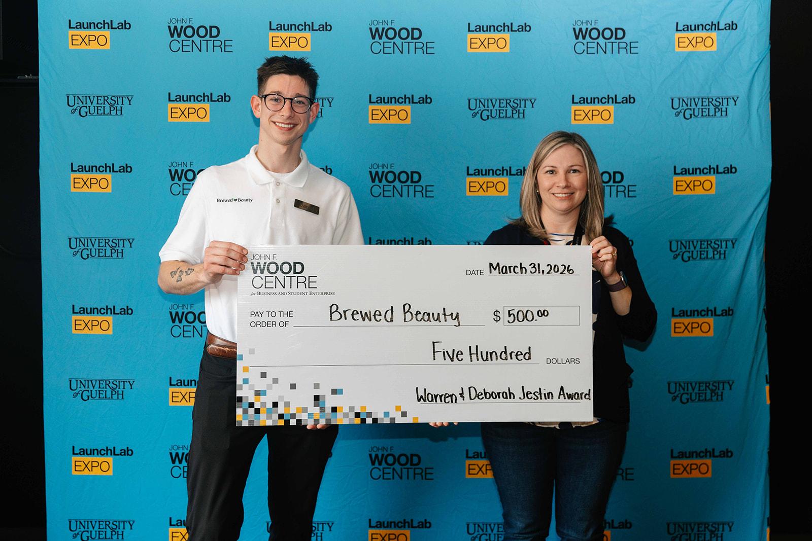 2 individuals holding a cheque with the text 'brewed beauty"