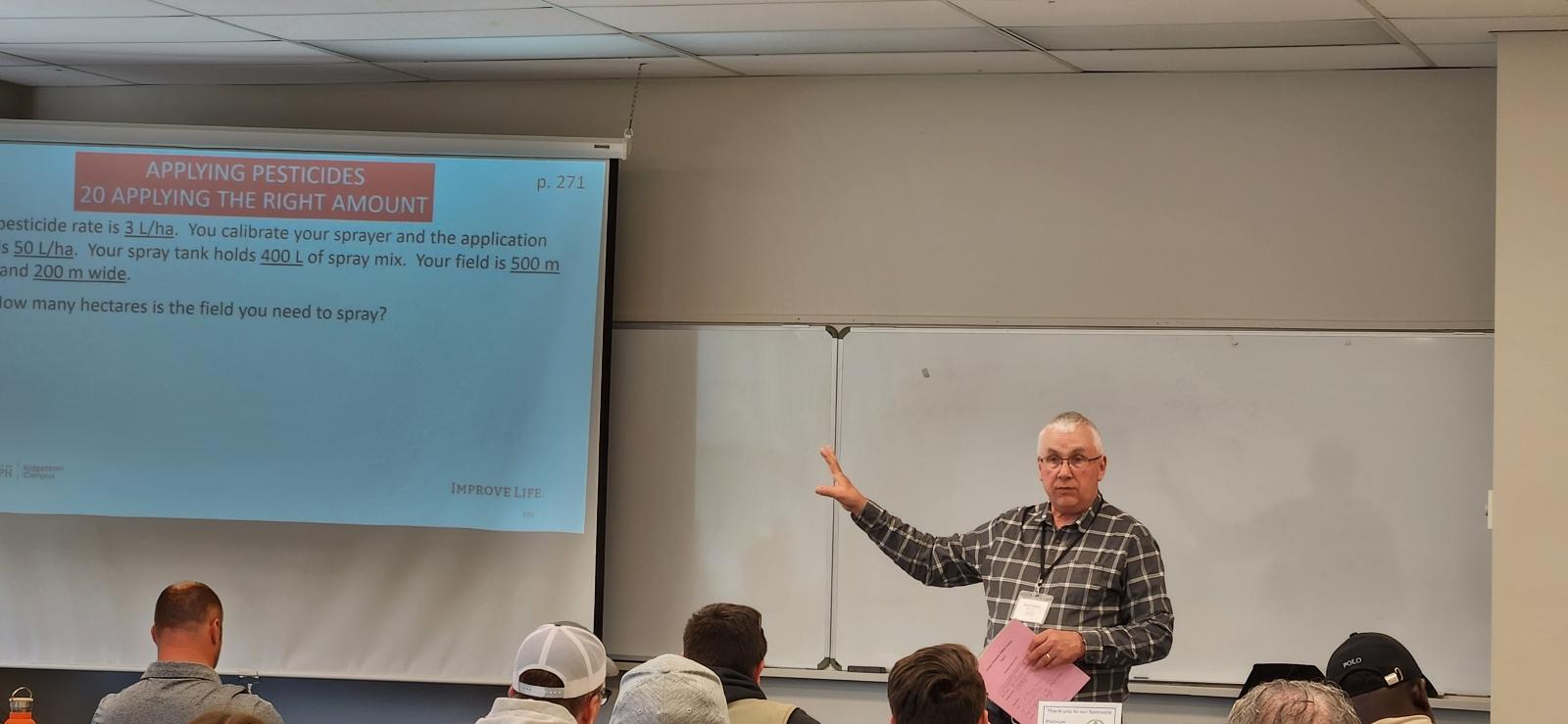 In a classroom, the instructor gestures to a slide projection while students listen.