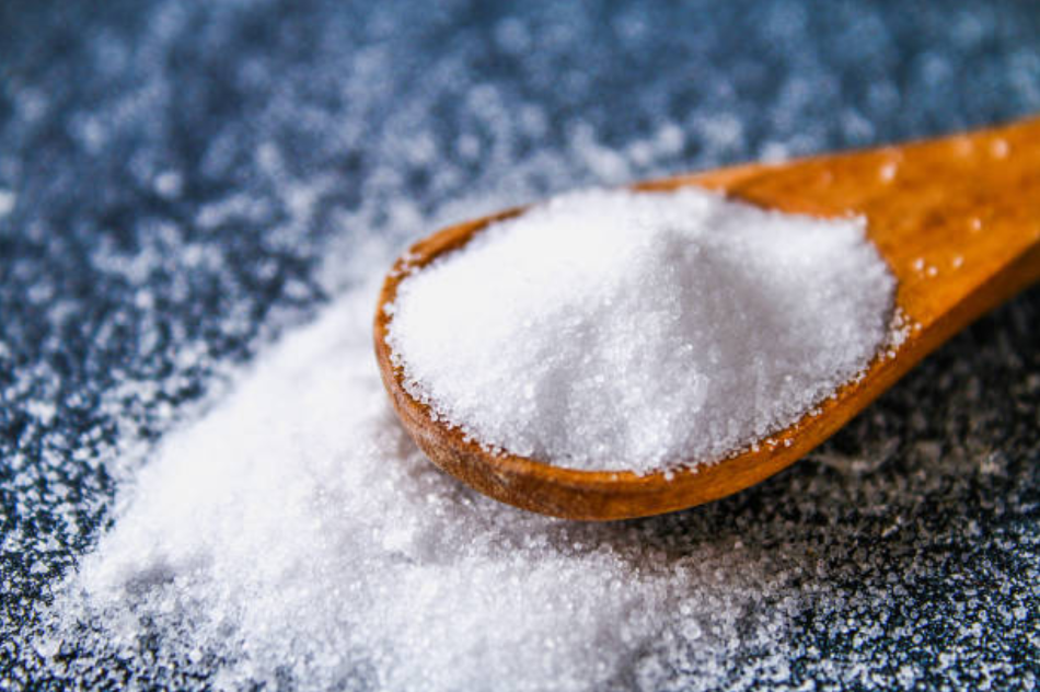 Table salt on a spoon, spilled on a blue table.