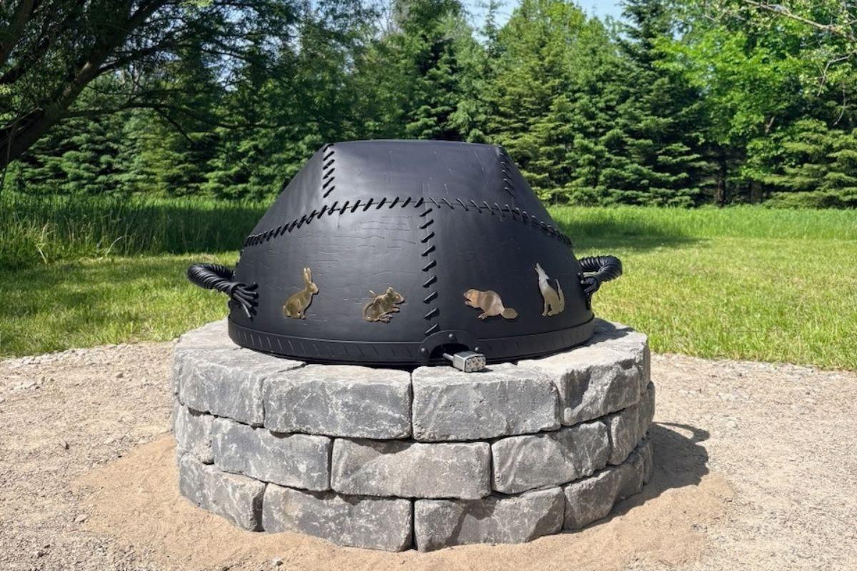 A circular, stone-lined Sacred Fire pit built into the grass at the University of Guelph Arboretum