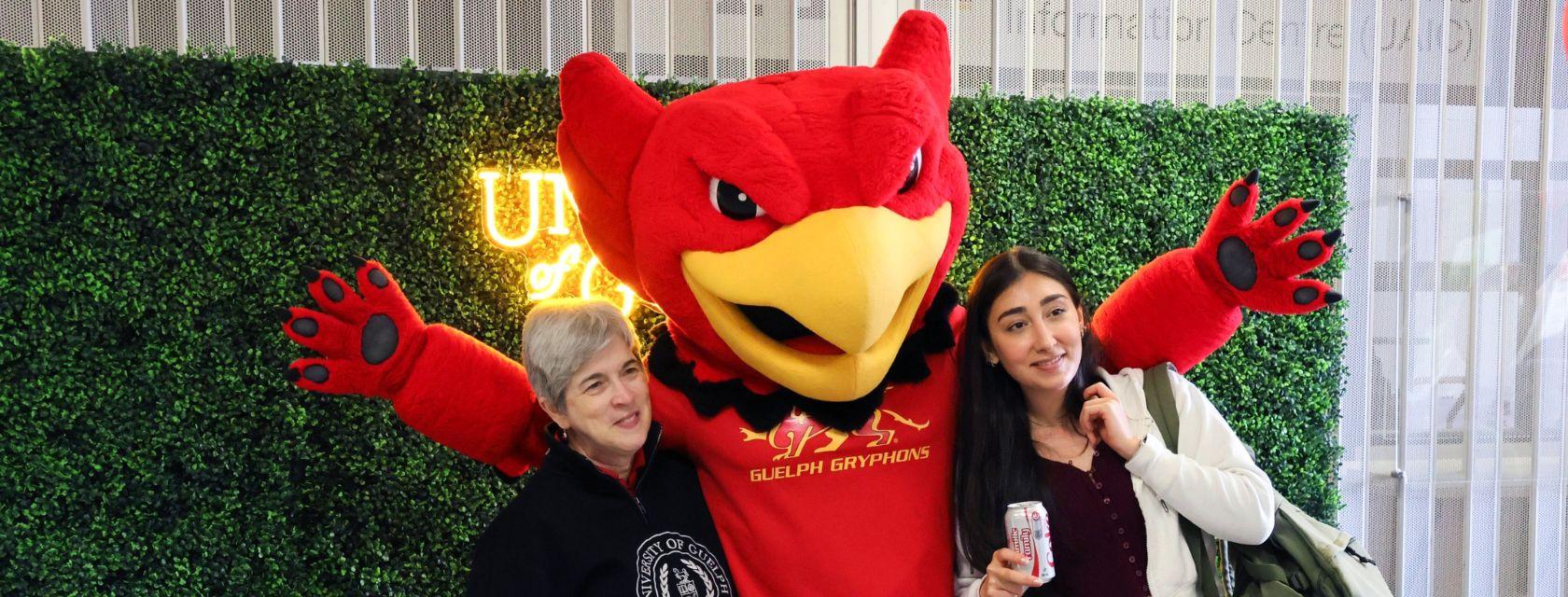 Two staff members pose for a photo with Gryph the U of G gryphon mascot