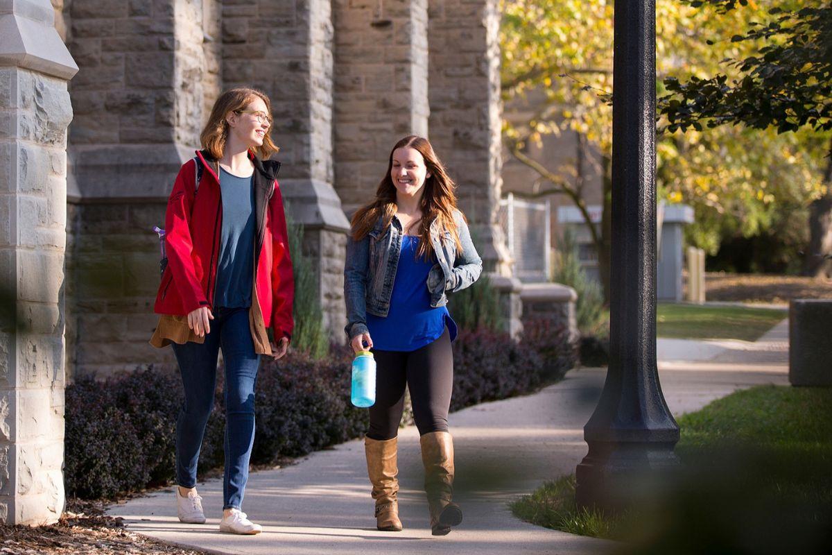 Two female students walking down a path on campus while talking